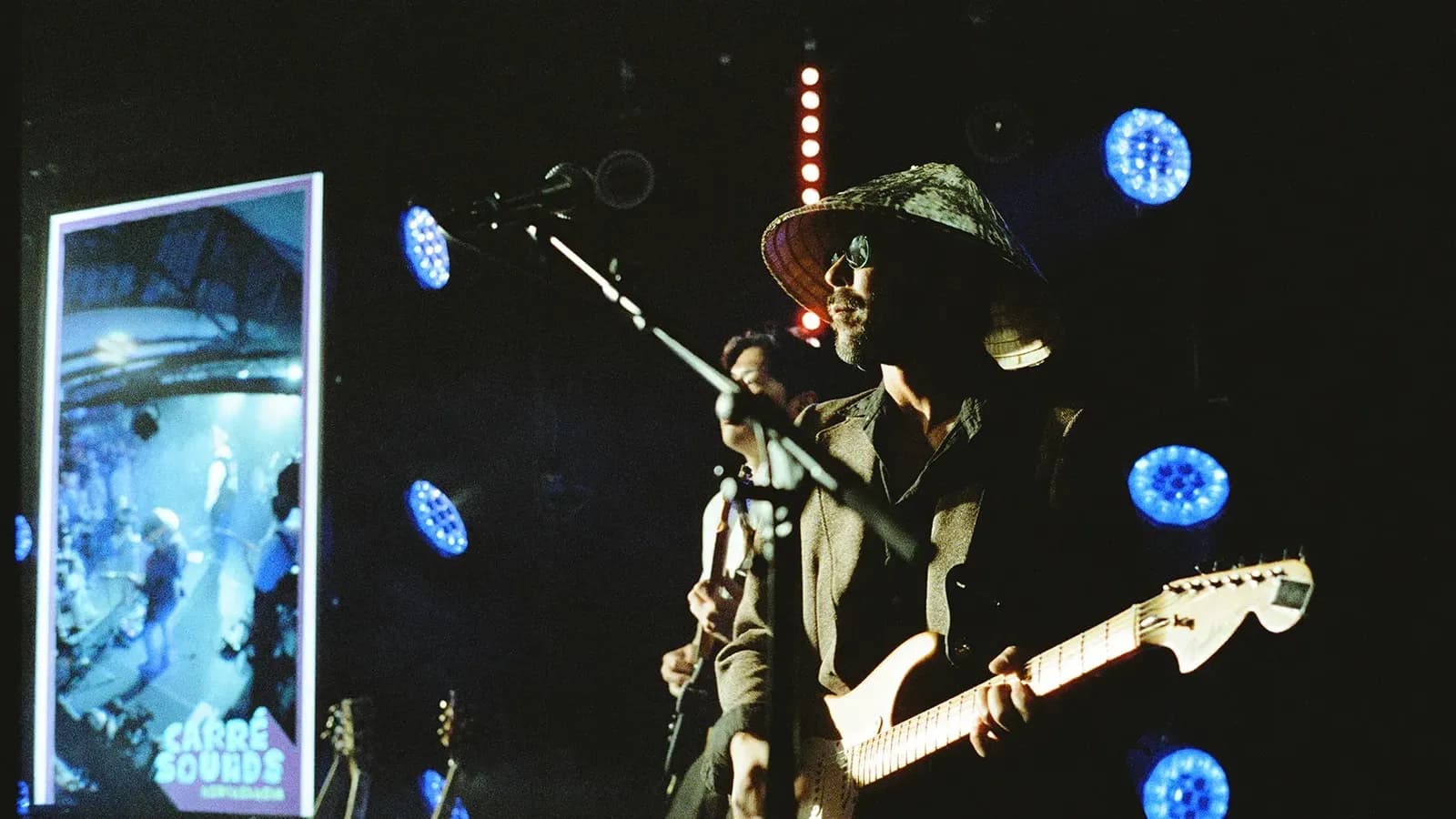 Gitarrist mit Hut im Gegenlicht, daneben die LED-Wand mit dem Carré-Sounds-Motiv