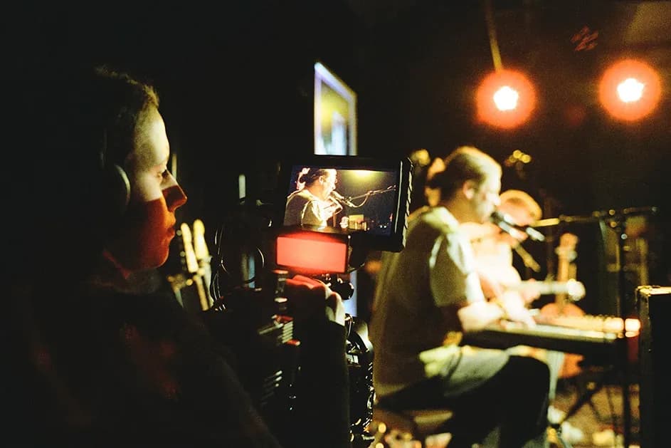 Kamerafrau mit Kopfhörern am Monitor, im Hintergrund ein Musiker an der Pedal Steel