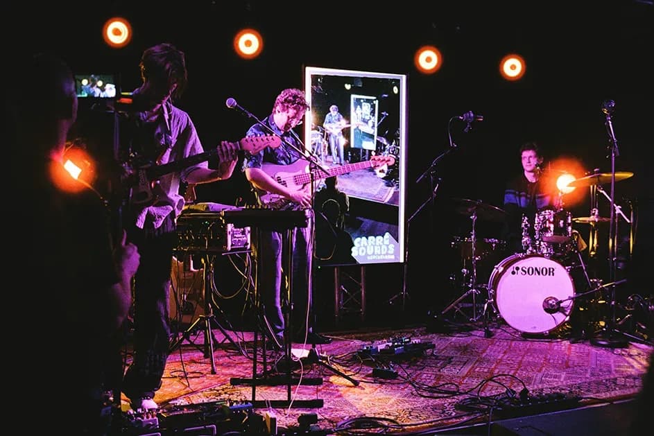 Dreiköpfige Band auf der violett beleuchteten Bühne, dahinter die LED-Wand mit dem Carré-Sounds-Logo