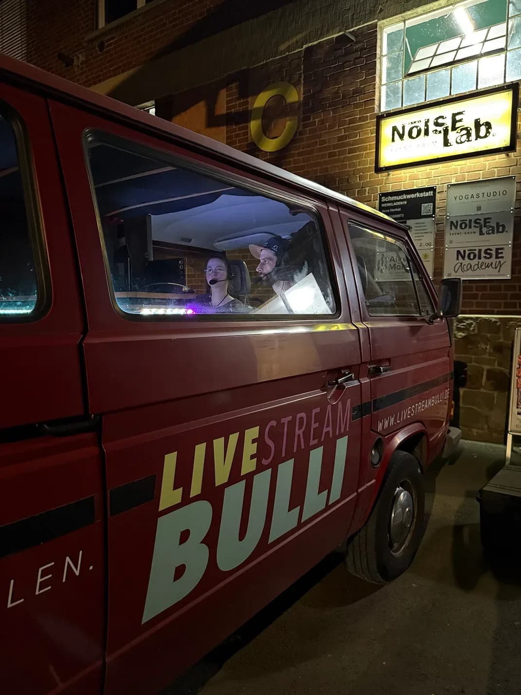Der Livestream-Bulli vor dem Eingang des Noise Lab, im Fahrzeug zwei Personen mit Headsets an der Regie